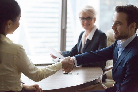 Businessman and businesswoman handshaking at group meeting, happy hr manager welcoming applicant at job interview hiring successful candidate, satisfied boss rewarding thanking employee shaking handsの写真素材