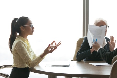 Serene asian businesswoman feeling zen meditating during stressful job meeting, calm office worker avoiding ignoring stress for emotional balance relief concept, female employee doing yoga at workの写真素材