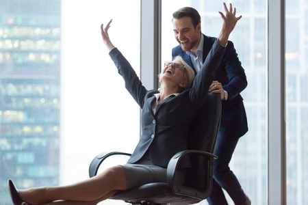 Happy carefree middle aged businesswoman enjoying funny office activity riding on chair, excited mature executives celebrate business success great relations having fun at work break feel free laughの写真素材