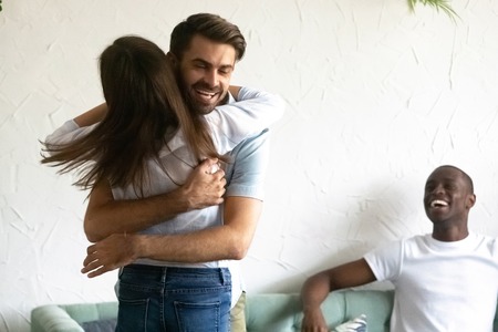 Diverse people gathered together in cafeteria or home, rear view young woman standing embracing with cheerful male people glad to see each other, friends showing care friendship and warm relationsの写真素材