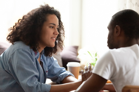 Mixed race girl looking with tender at African American boyfriend, young couple in love dating in coffeehouse, drinking coffee, spending weekend together, having pleasant conversationの写真素材