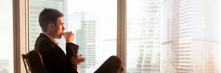 Horizontal photo businessman sitting on chair drink coffee look window at big city modern buildings rest after work. Vision motivation concept banner for website header design with copy space for textの写真素材