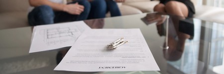 Horizontal photo couple and sitting on sofa, close up focus on agreement paper and keys on glass table, buy sell property, long-term tenancy relocation concept banner for website header designの写真素材