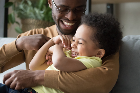 Affectionate loving african dad holding tickling child toddler son, happy playful black father and mixed race kid boy embracing having fun laughing cuddling enjoy positive emotions playing togetherの写真素材