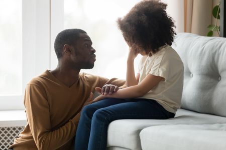 Loving african american dad comforting crying sad kid daughter holding hand supporting little stressed school girl in tears, black father consoling talking to upset child giving empathy protectionの写真素材