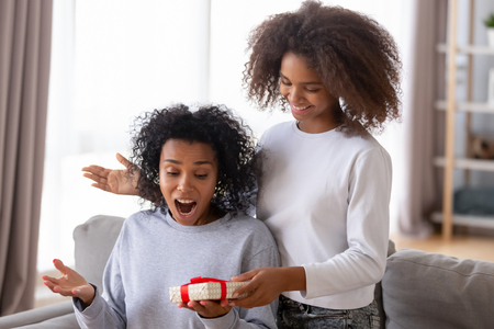 Mixed race excited mommy received from teenager daughter gift box feels happy. Adolescent younger sister make surprise presenting handmade package. Celebration of life events and mother day conceptの写真素材