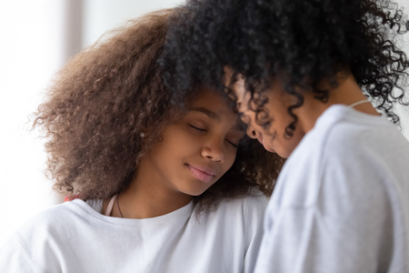 Mixed race loving mommy and teen daughter close to each other touching foreheads with closed eyes enjoy time together, tender moment strong connection, bonding, family relative people and love conceptの写真素材
