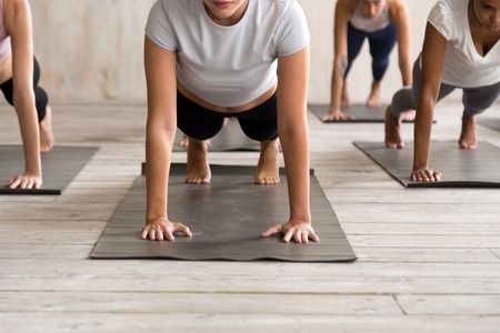 Group of young diverse sporty people practicing yoga, doing Push ups press ups exercise, phalankasana, Plank pose, hands close up, active students training at sport club or studio. Well being conceptの写真素材