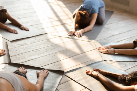 Group of diverse young sporty people at yoga lesson, doing Child exercise, Balasana pose, mixed race female students training indoor at club or studio. Well being, wellness concept, close up. Top viewの写真素材