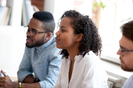 Specialists, profile side view, sitting during business seminar listening presentation, focus on black mixed race young business lady. Meeting of client and representatives or study of company staffの写真素材