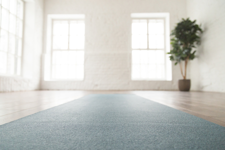 Close up unrolled yoga mat on wooden floor in empty room, modern yoga studio or fitness center with big windows and white brick walls, sport equipment for meditating or exercisesの写真素材