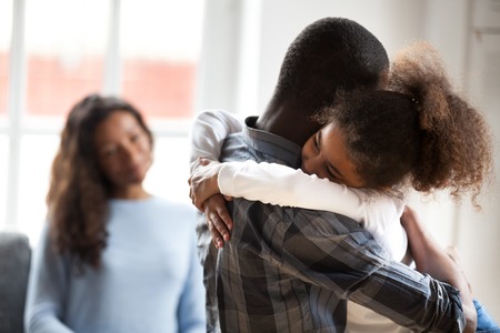 Cute little preschool African American daughter hug young father showing love and care, smiling small child girl embrace black father happy to spend time with parents at home. Family wellbeing concept