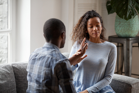 Young mixed race couple sit on couch arguing blaming each other for cheating, black husband and wife fight at home proving point of view, close to divorce or separation. Relationship problem concept