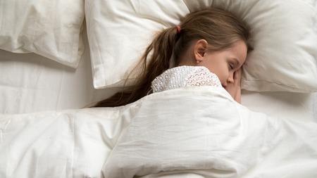 Adorable cute little baby girl sleeping alone in comfortable bed lying on soft pillow covered with...