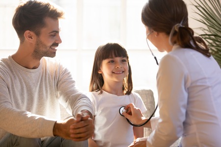 Paediatrician holding device stethoscope listening heart sounds lungs of little girl, father daughter during health examination, general health checkup in hospital, children medical insurance conceptの写真素材