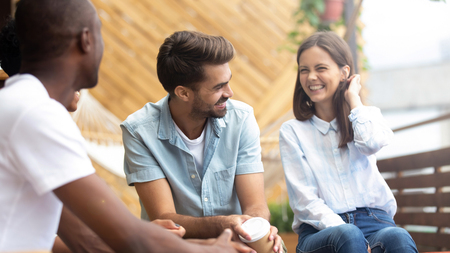 Multicultural happy people laughing at funny joke talking at reunion meeting on cafe terrace outdoor, cheerful diverse friends having fun drink coffee enjoy laughter, multi-ethnic friendship hangoutの写真素材