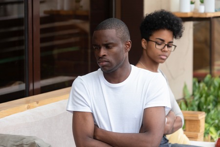 Angry jealous upset african american man ignore avoid sad wife sitting turned back outdoor, sad annoyed black husband disappointed in bad marriage, family couple fights and problems in relationshipsの写真素材