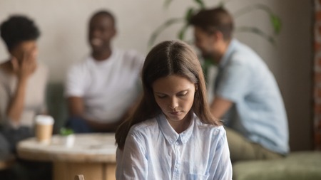 Upset offended bullied young girl sitting alone in cafe, depressed sad lonely teen student excluded by bad friends, female outcast introvert feeling hurt outsider loser suffer from unfair attitudeの写真素材