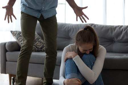 Unhappy frightened woman crying, sitting on floor, aggressive man shouting to scared wife, angry husband emotionally quarreling, arguing, emotional psychological abuse, domestic violence conceptの写真素材
