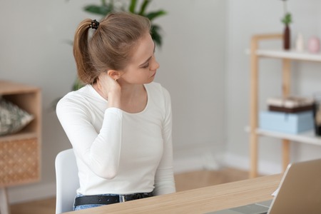 Tired woman feeling pain after sedentary computer work in uncomfortable posture or office chair, exhausted female student or employee massaging tensed neck muscles, sitting at workplaceの写真素材
