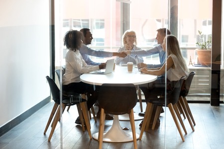 Happy diverse businessmen handshake at group meeting negotiation in boardroom make business deal agreement with client thank partner for collaboration sit at conference table shake hands behind glass.の写真素材