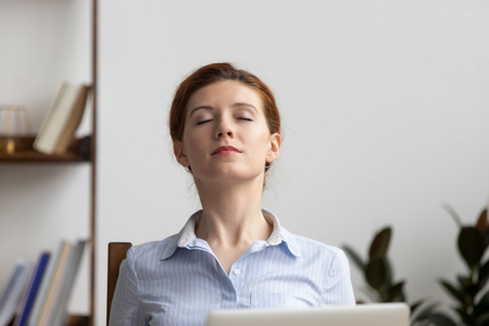 Relaxed calm business woman take deep breath of fresh air resting in chair lounge with eyes closed at work in office, serene happy female employee meditate feeling no stress free relief at workplaceの写真素材