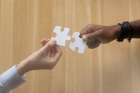 Two diverse black and white male female people hands holding join jigsaw puzzle missing piece, connected couple love finding best match in relationships and partnership concept, top close up viewの写真素材