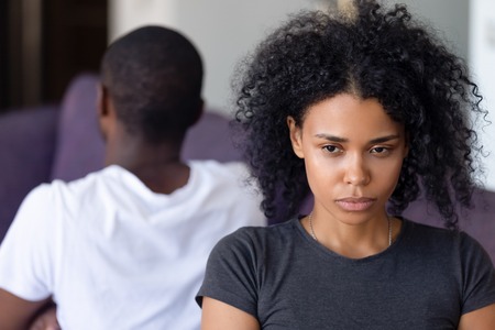 Close up sad frustrated African American woman after family quarrel with man, sitting separately on sofa, ignoring each other, offended upset wife avoid talking with husband, misunderstandingの写真素材