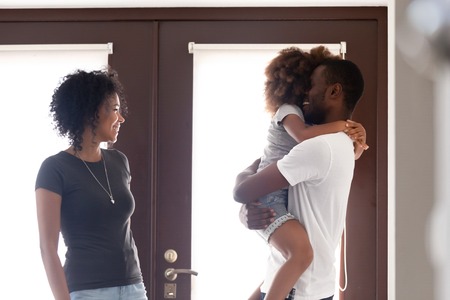 African American man arrived home after long business trip, happy family reunion, loving father holding little daughter in hands, cuddling, smiling wife standing near in hall, celebrate returnの写真素材