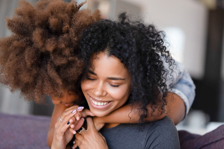 Close up smiling African American mother embracing with preschool daughter, sitting in living room on cozy sofa at home together, feeling happy, family warm relationships, showing support and love