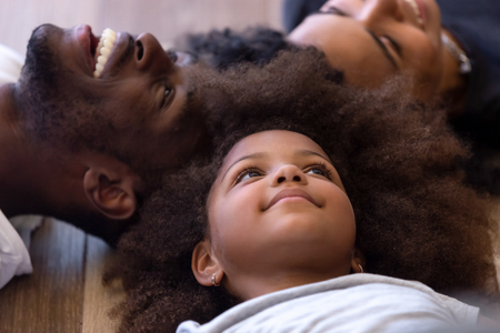 Close up happy African American family lying on warm floor together, feeling happy, smiling handsome father and mixed race mother spending free time, weekend with adorable little daughterの写真素材