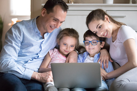 Happy family with kids watching funny video on computer screen. Mother, father, daughter and son...