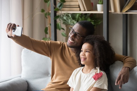 African father raise hand hold smartphone sitting with little biracial daughter take self portrait...