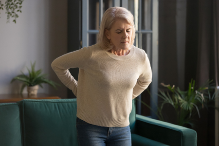 Unhappy grey haired mature woman with closed eyes touching, massaging back, tired sad middle aged...