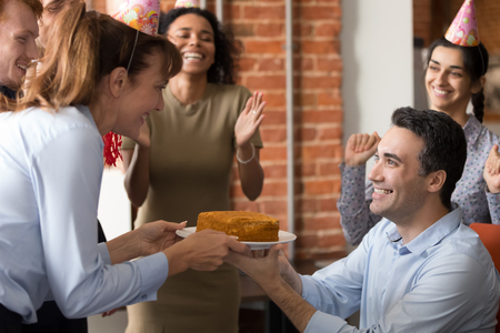 Excited multiracial work team congratulate male coworker with birthday making surprise throw party, happy diverse employees have fun laugh greeting colleague presenting cake celebrating in officeの写真素材