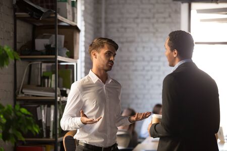 Diverse friends two businessmen standing at office distracted from work take break drink coffee having informal talk, boss employee planning new project discuss interesting idea companionship conceptの写真素材