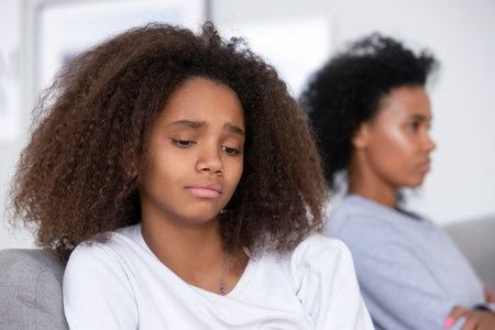 Unhappy African American teen girl having problem with strict mother, upset stubborn mum and unhappy teen girl child ignoring to each other, not talking after quarrel, family generation conflictの写真素材