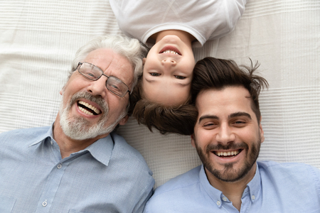 Top view of happy three generations of men lying on bed looking at camera making photo together,...