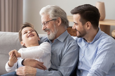 Loving grandfather cuddle hug smiling preschooler boy relax together at home, three generations of...