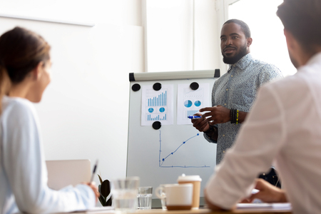 Black male leader coach standing near whiteboard answering questions of business team members. Corporate training coaching course, group business meeting, discussion of development strategy conceptの写真素材