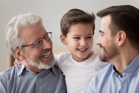 Close up of smiling preschooler boy child hug father and grandfather spend time together at home,...