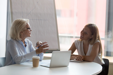 Mature businesswoman mentor talking with female intern in boardroom, explaining task to trainee, discussing business strategy, staff training concept, brainstorming, employee consulting clientの写真素材