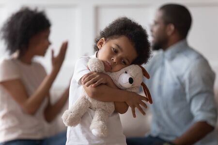 Sad little african child boy embrace toy upset by parents arguing, stressed lonely innocent small black kid son feel hurt having psychological trauma suffer from family conflicts, parents divorceの写真素材