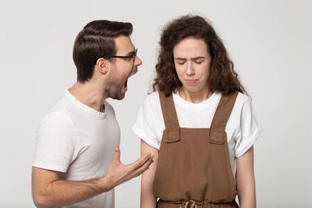 Young unhappy couple isolated on grey studio background, mad angry guy open mouth screaming at girlfriend, girl standing desperate listening aloud yelling feels weak abused crying unable to fight backの写真素材