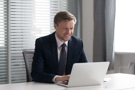 Smiling male ceo entrepreneur in suit working on computer sit at office desk, happy businessman...