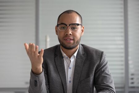 Serious african businessman entrepreneur in suit talking to camera, mixed race coach webinar speaker teacher trainer shooting vlog online business training look at webcam make conference video callの写真素材