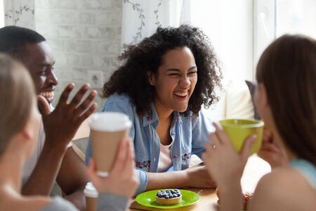 Overjoyed mixed race young curly woman laughing on best friends joke at diverse people meeting in...