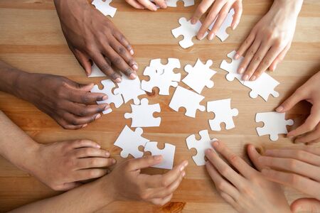 Close up top above view diverse male and female hands assembling puzzles together on table. Multiracial connection, logical thinking, students teamwork cooperation, business strategy concept.の写真素材