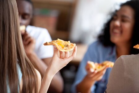 Close up image of caucasian young woman holding slice of delicious pizza, excited happy mixed race...