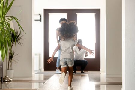 African family having fun in hallway, daughter missed her parents running to mom and dad standing in the doorway of modern house. Family reunion, mortgage happy homeowners arrived a new home conceptの写真素材